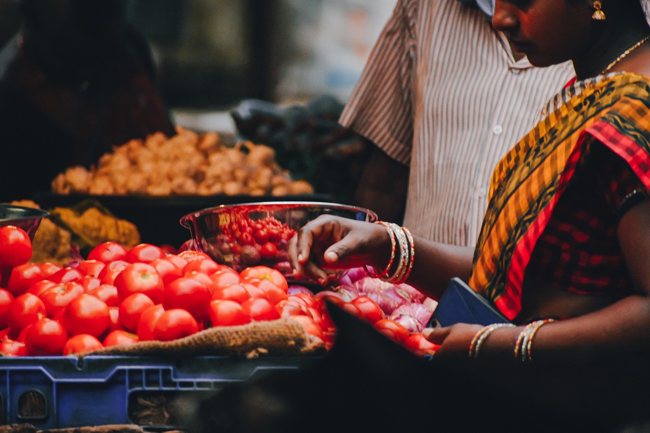 A trader sorting tomatoes and onions at a busy market stall, one seller among many where the customer only stops at one
