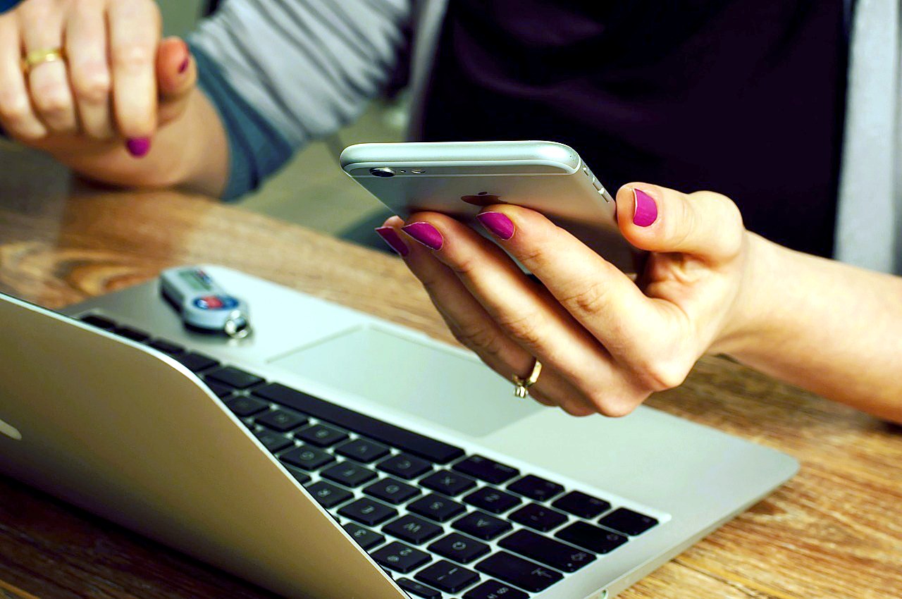 A woman's hands holding a phone above an open laptop on a wooden desk, the moment an owner checks why fewer customers are calling