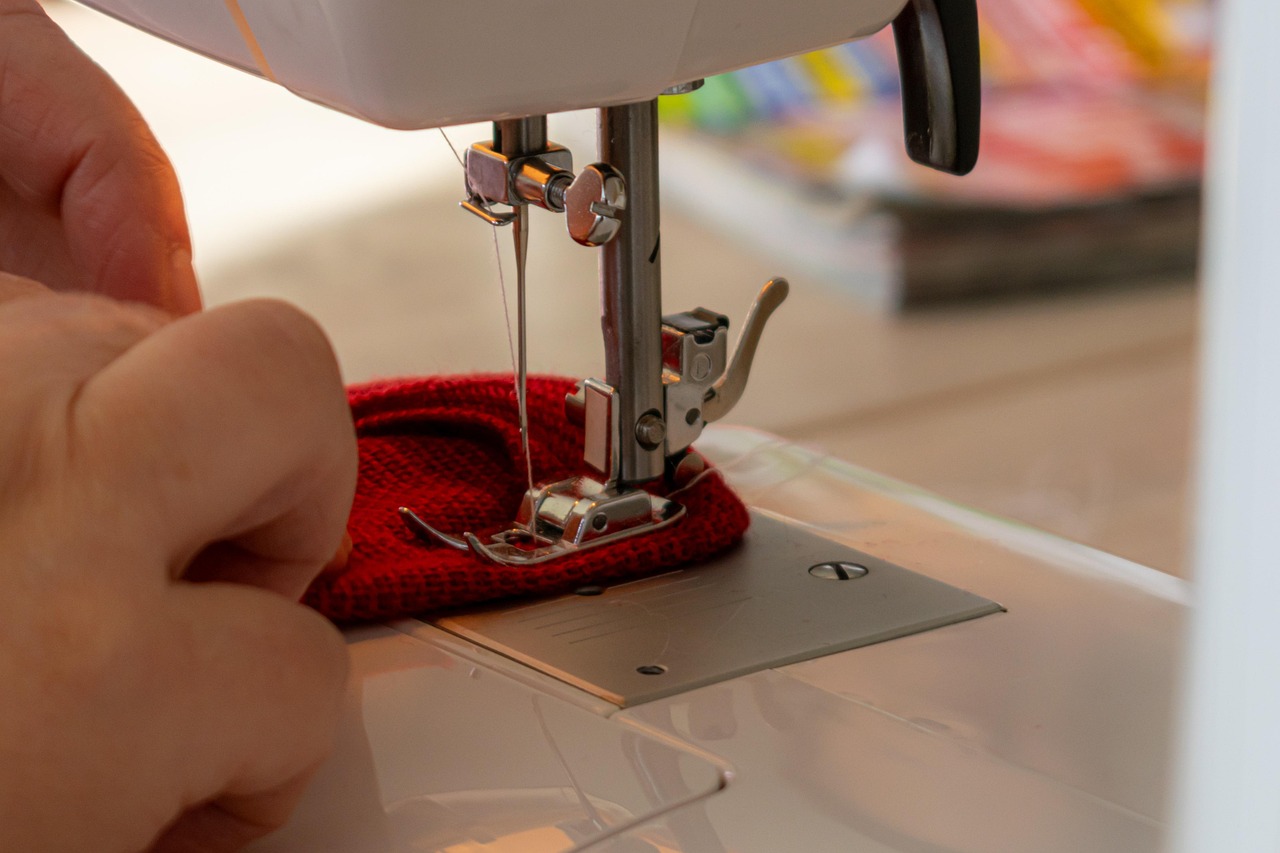 A tailor's hands guide red fabric under the needle of a sewing machine, the kind of small business the Loop is run for