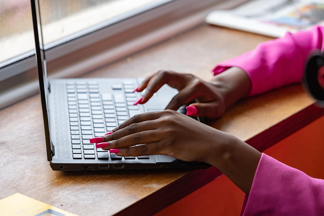 A woman's hands type a customer question into a laptop at a bright desk by a window, recording which businesses the answer names