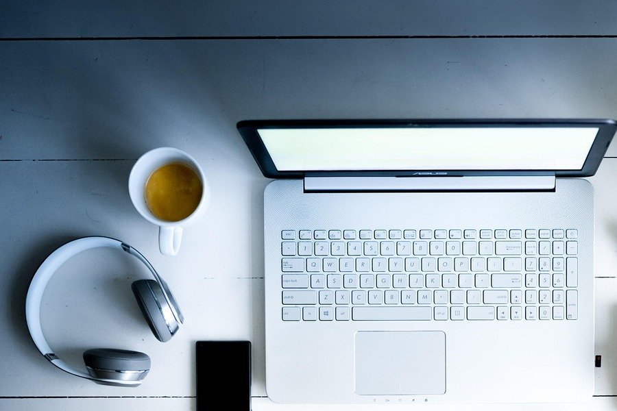 A laptop open on a white wooden desk beside a cup of tea, headphones and a phone, the desk where an owner checks Google rankings and ChatGPT answers