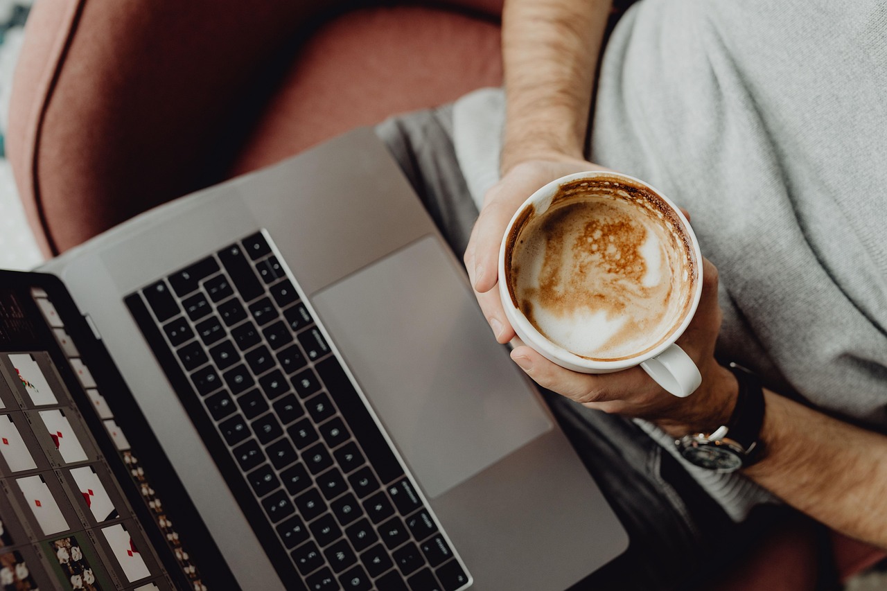 An owner holding a cup of coffee looks down at an open laptop, checking the website in a browser, where every page looks finished